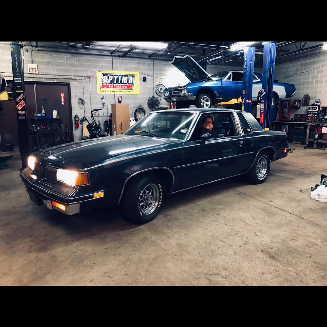 Nefty sitting proudly inside the dark green 1987 Oldsmobile Cutlass Supreme at his shop in Addison, Illinois